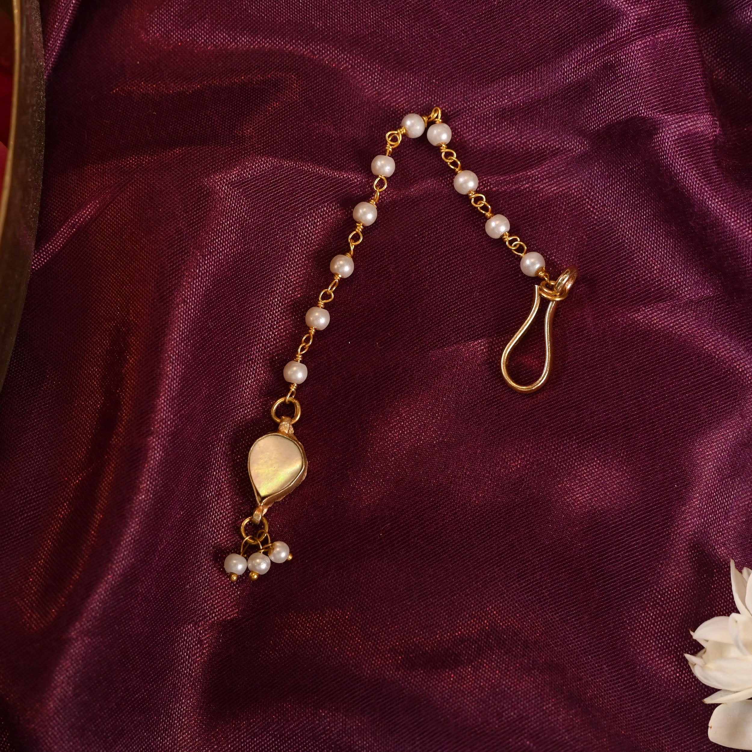 Gold plated jadau kundan maang tika with pearl and semi-precious stones on a copper base, displayed on a purple fabric background.