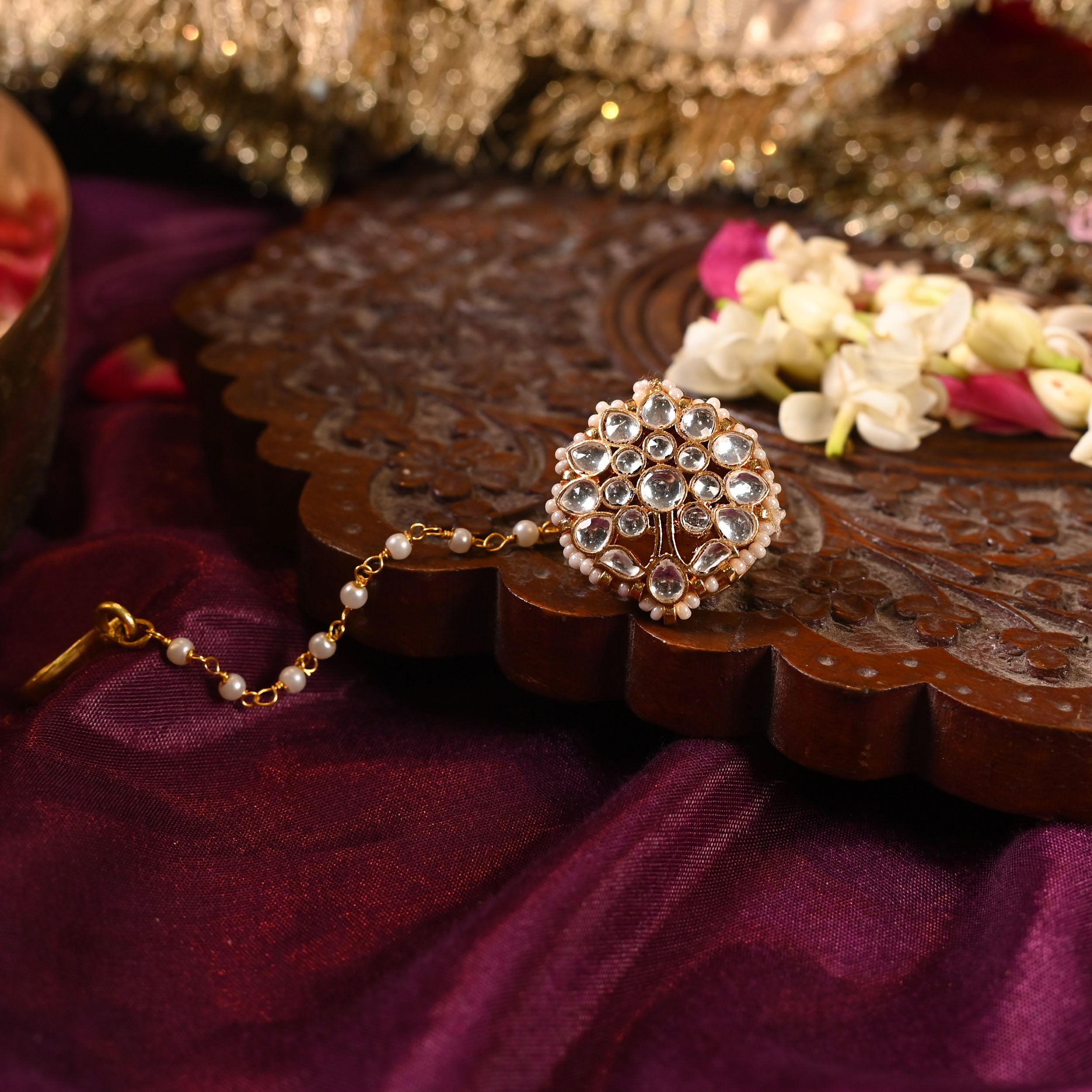 A gold-plated Jadau Kundan Borla with semi-precious stones set in copper, with silver foil in 18k gold plating, displayed on a wooden surface.